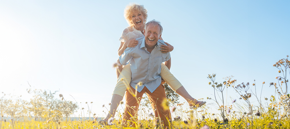 Happy senior man laughing while carrying his partner on his back in the countryside