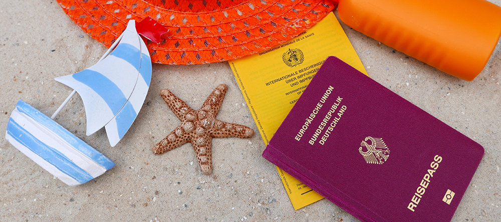 Reisepass mit Impfausweis Sonnenhut und Sonnenlotion am Strand